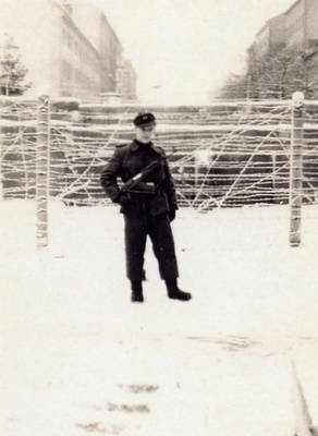 Bewaffneter Grenzsoldat posiert auf Ackerstraße vor Stacheldrahtzaun und Mauer